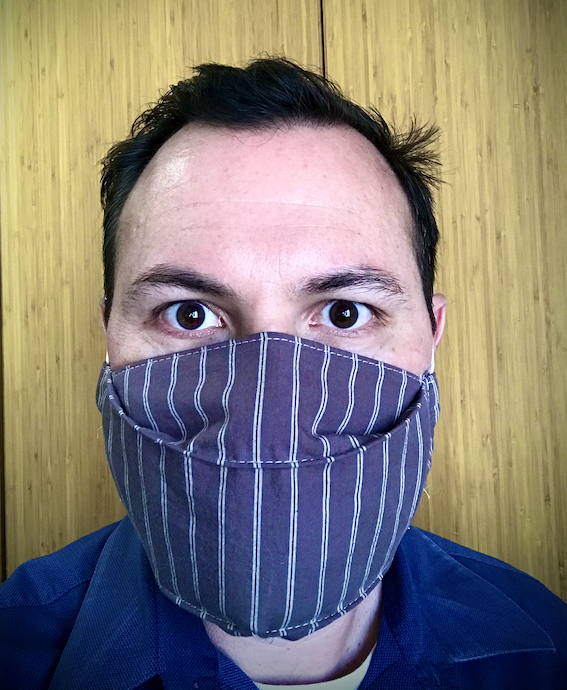 Bill Selak selfie wearing a blue striped mask against a wooden background